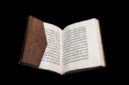 An ancient Quran manuscript with Arabic calligraphy and leather binding. The historic Islamic manuscript is displayed open against a black background.