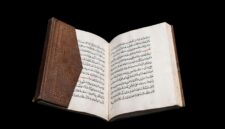 An ancient Quran manuscript with Arabic calligraphy and leather binding. The historic Islamic manuscript is displayed open against a black background.